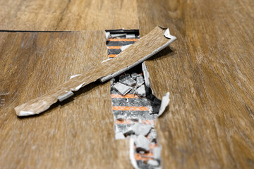 exposed heating cable under damaged laminate, installer assessing repair needs, torn planks with visible foil heating mat, adhesive residue and broken surface, interior