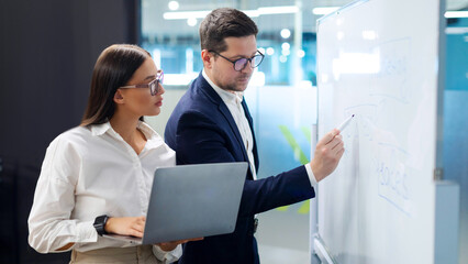 Successful colleagues meeting and talking about business, making project, employees discussing solution on whiteboard and using laptop