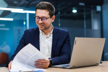 Businessman in office working with documents, analyzing paperwork, desk equipped with laptop and papers, sitting at workplace in office