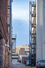 Alley view between buildings featuring a metal fire escape during daylight