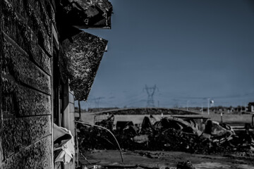Burnt remains of a building in a rural landscape after a fire on a clear day with power lines in the background