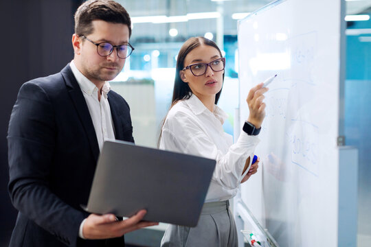 Creative business people meeting together and thinking on new business ideas in office board room, standing near whiteboard with laptop. Analysis chart presentation