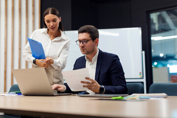 Obraz premium Businessman and businesswoman assistant working with documents, looking at laptop and discussing project during meeting in board room in office, copy space