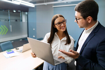 Friendly colleagues chatting in office board room, discussing project ideas, female employee consulting with male mentor showing presentation on laptop