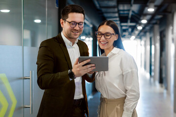 Business professionals interacting in office environment, engaging with digital tablet, discussing ideas, technology, emphasizing teamwork, office hall interior