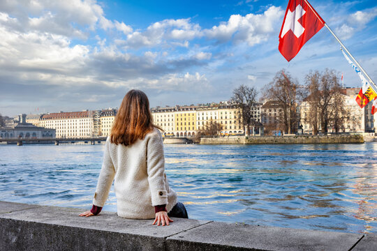 A tourist woman looks at the beautiful view of the cityscape of Geneva, Switzerland, with River Rhone and lake during a sunny winter day