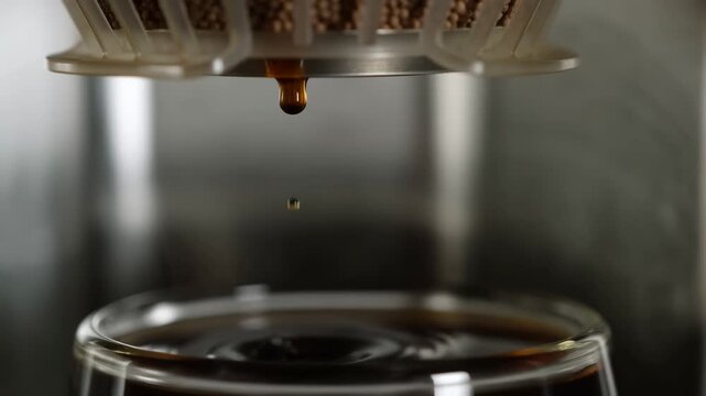 Coffee dripping into glass cup: brewing process in closeup slow motion