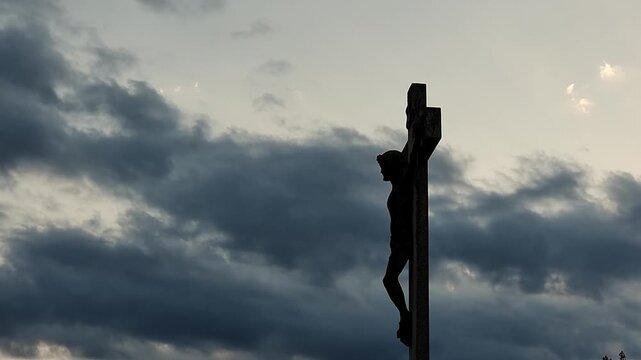 Stone statue representing Jesus Christ crucifixion, at sunset, 4K clouds time lapse