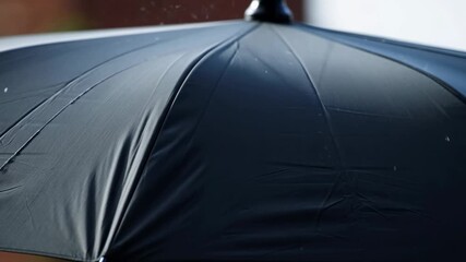 Closeup of rain falling on a dark umbrella in slow motion