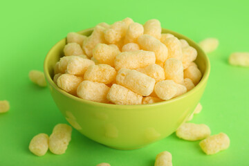 Bowl with sweet corn sticks on green background, closeup