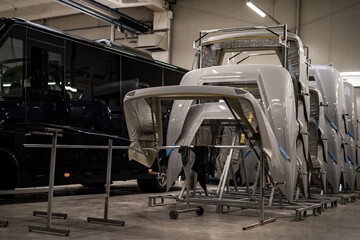 Industrial vehicle manufacturing workshop with metal bus frames and body structures under assembly. Large factory interior shows fabrication, welding, and custom vehicle production in progress.