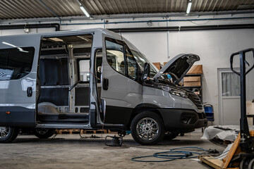 Industrial vehicle manufacturing workshop with metal bus frames and body structures under assembly. Large factory interior shows fabrication, welding, and custom vehicle production in progress.
