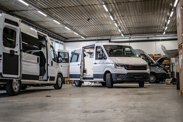 Commercial vans in industrial workshop during conversion and assembly. Vehicle interiors exposed,...