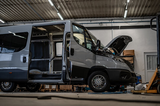 Commercial vans in industrial workshop during conversion and assembly. Vehicle interiors exposed, doors open, showing custom transport production, maintenance, and manufacturing process.
