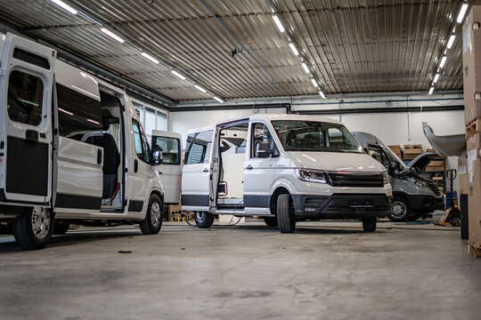 Commercial vans in industrial workshop during conversion and assembly. Vehicle interiors exposed, doors open, showing custom transport production, maintenance, and manufacturing process.