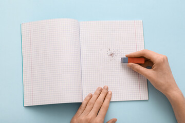 Woman erasing something in notebook on blue background