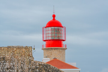 Bright red lantern of the Cape St. Vincent lighthouse stands against a cloudy sky.