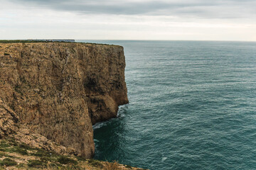 Steep vertical rock wall meets the calm ocean under a soft overcast sky.