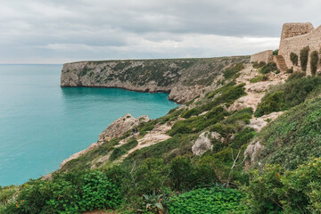 A rugged coastal path winds past ancient stone walls overlooking Atlantic ocean.