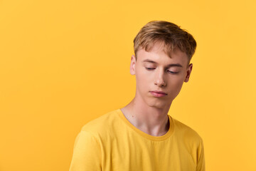 Fototapeta premium Young male in a yellow t shirt against a bright yellow backdrop, conveying calm, thoughtful mood with soft lighting for a minimalist studio look and modern fashion vibe