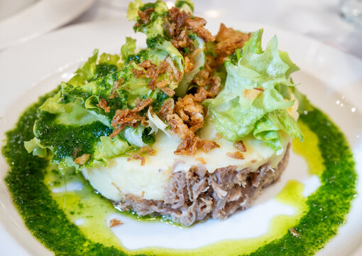 French dish parmentier of candied duck, shredded canard confit with potatoes puree and green pesto, served in traditional bistro bouillon restaurant in Paris