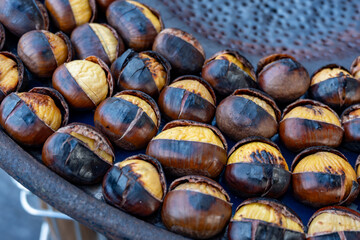 Traditional vintage French equipment for roasting and grilling fresh chestnuts over open fire, delicious street food, eating nuts on streets of Paris in autumn