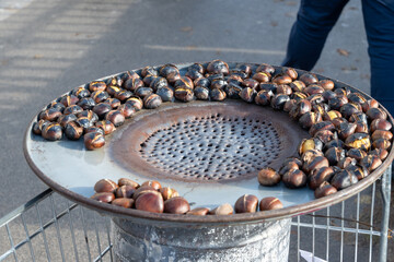 Traditional vintage French equipment for roasting and grilling fresh chestnuts over open fire, delicious street food, eating nuts on streets of Paris in autumn