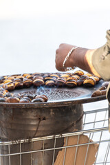 Traditional vintage French equipment for roasting and grilling fresh chestnuts over open fire, delicious street food, eating nuts on streets of Paris in autumn