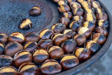 Traditional vintage French equipment for roasting and grilling fresh chestnuts over open fire, delicious street food, eating nuts on streets of Paris in autumn