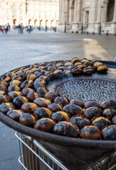 Traditional vintage French equipment for roasting and grilling fresh chestnuts over open fire, delicious street food, eating nuts on streets of Paris in autumn