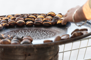 Traditional vintage French equipment for roasting and grilling fresh chestnuts over open fire, delicious street food, eating nuts on streets of Paris in autumn