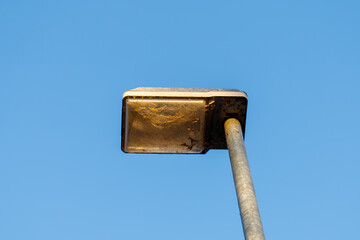 Old street lamp with dust and cobwebs against blue sky