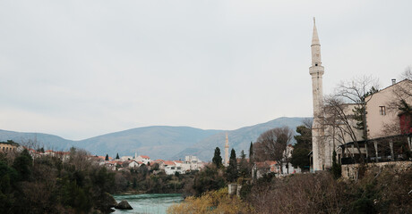Obraz premium Old town of Mostar with mosque, minaret, historic houses, and turquoise Neretva River. Cultural Balkan cityscape representing history, religion, and travel heritage.
