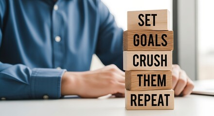 Man in blue shirt with wooden blocks spelling SET GOALS CRUSH THEM REPEAT.