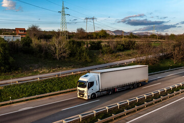 Transportation truck with semi-trailer driving along highway on the sunset background. Services and...