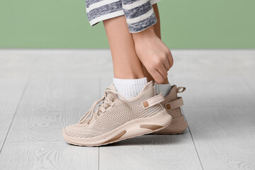 Cute little girl putting on stylish beige sneakers near green wall, closeup