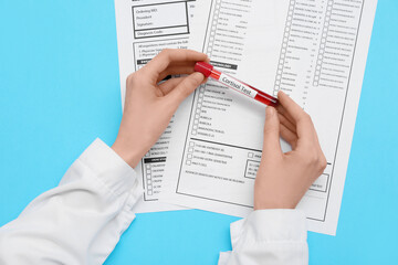 Female doctor's hands with blood sample of cortisol and laboratory test forms on blue background. Medical concept © Pixel-Shot