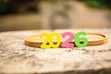 Colorful 2026 wooden numbers on a tray over a stone surface with lush green bokeh. Perfect for New Year 2026 and future planning themes