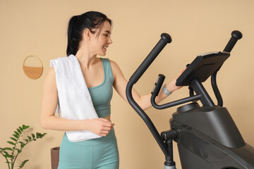 Sporty young woman with towel near modern exercising bike in stylish gym