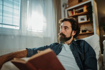 Thoughtful man reading book, relaxing in living room