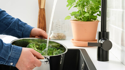 Person washes broccoli in a kitchen sink with running water while preparing for cooking.