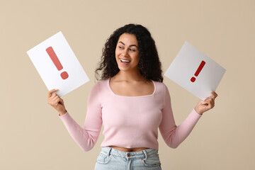 Happy young African-American woman holding paper sheets with exclamation marks on beige background