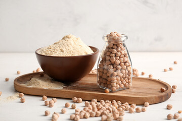 Bowl of chickpea flour and jar with beans on white wooden table