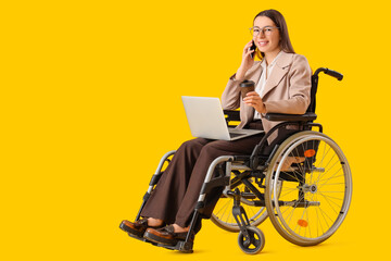 Young female businesswoman with laptop  talking by phone in wheelchair on yellow background. Equality concept