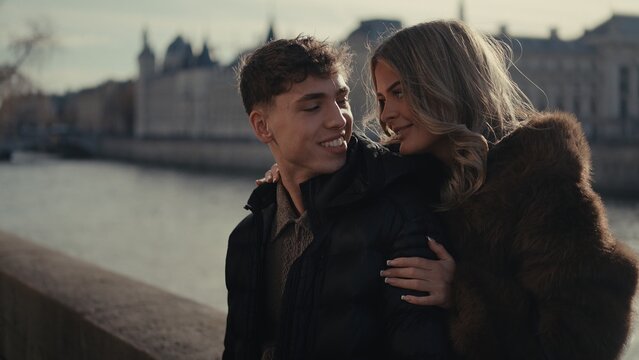 A romantic couple embraces in Paris France with the Seine River and city buildings in the background on a sunny day. This image is suitable for travel tourism and relationship concepts.