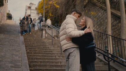 A young couple embraces on the steps of Montmartre in Paris France. This image can be used for travel romance or lifestyle content.
