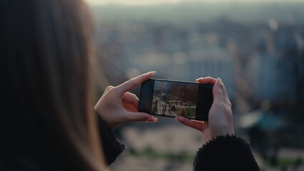 A woman is taking a photo with her smartphone of the Luxembourg Gardens in Paris France. This image can be used for travel tourism and urban lifestyle concepts.