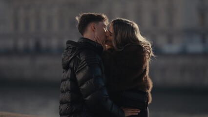 A romantic couple kisses with love and affection in Paris France on a sunny day The stylish couple is enjoying their time together in an urban setting with beautiful architecture.