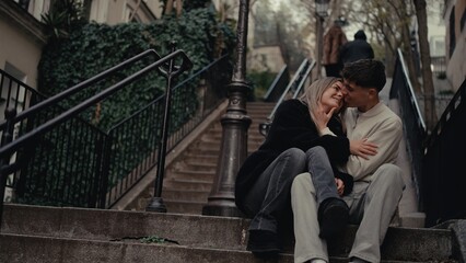 A young couple embraces on the steps of Montmartre in Paris France enjoying an intimate moment together. This image is perfect for illustrating travel relationships and the romance of a European city 