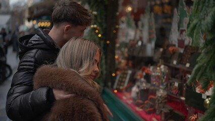 A romantic couple embraces while looking at a Christmas market window display in Paris France during the winter season The display features chocolate and holiday decorations creating a festive and lov
